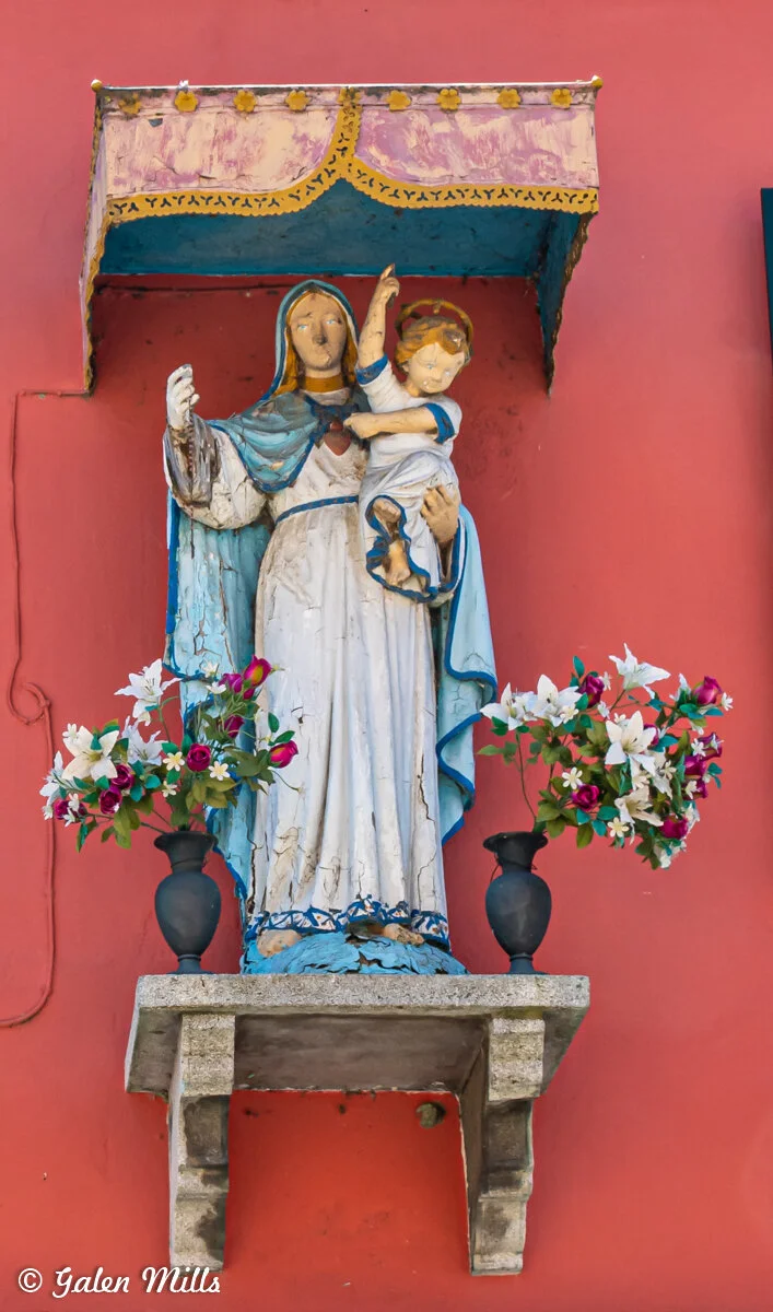 Statue of Madonna and Child surrounded by flowers, set against a red wall