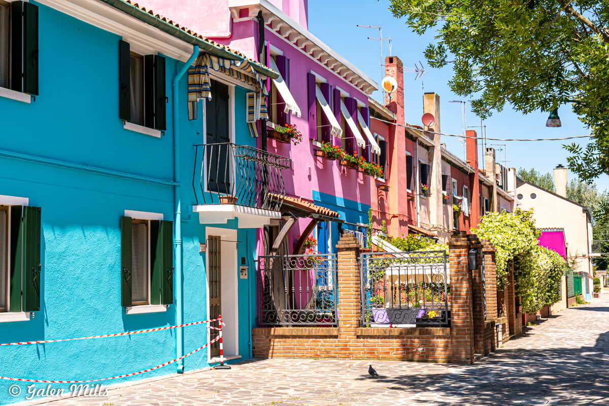 Colorful row of houses with blue, pink, and orange facades in Burano, Italy.