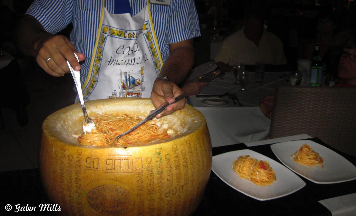 Person preparing pasta in a large wheel of cheese at a restaurant, serving it onto plates.