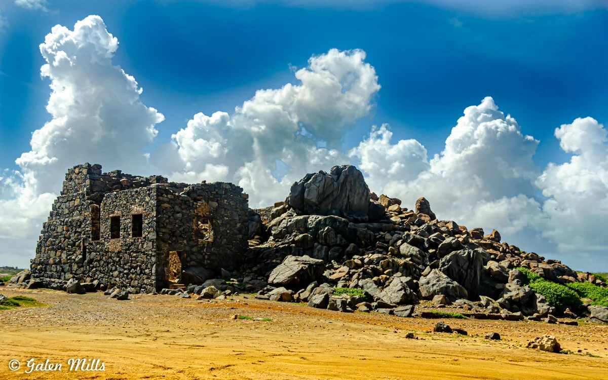 Stone ruins and boulders under a bright blue sky with fluffy clouds.