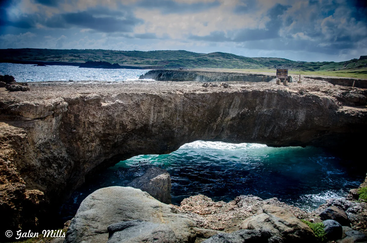 Coastal rock formation with natural bridge over ocean water, clear sky above
