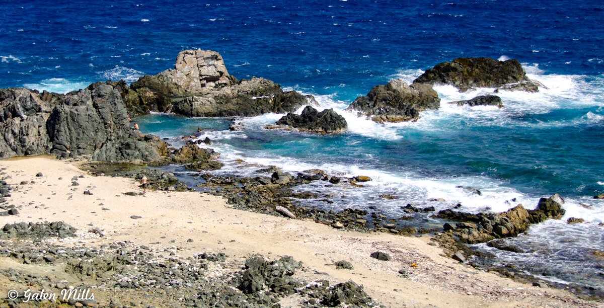 Rocky beach with ocean waves and blue sea under a clear sky.