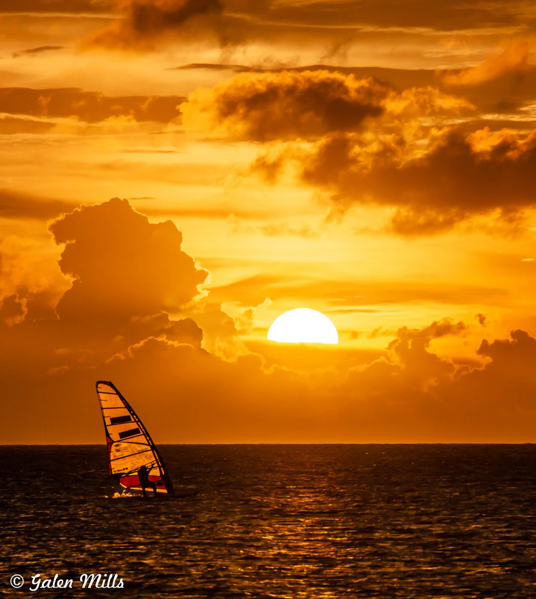 Windsurfer on ocean at sunset with orange sky and clouds
