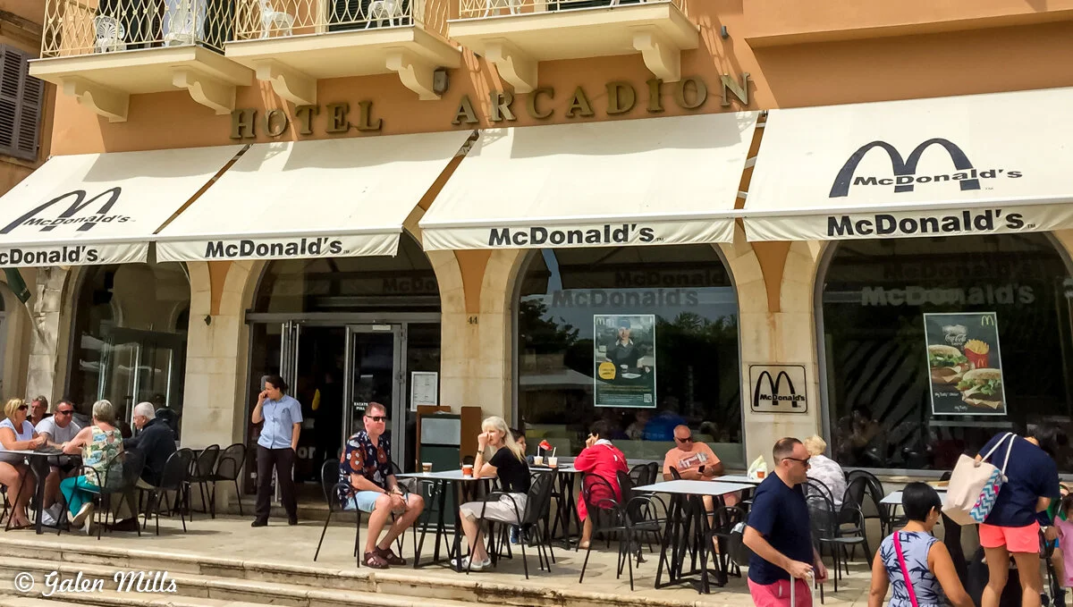 Outdoor seating area at a McDonald's restaurant located at Hotel Arcadion, with people dining at tables under umbrellas.