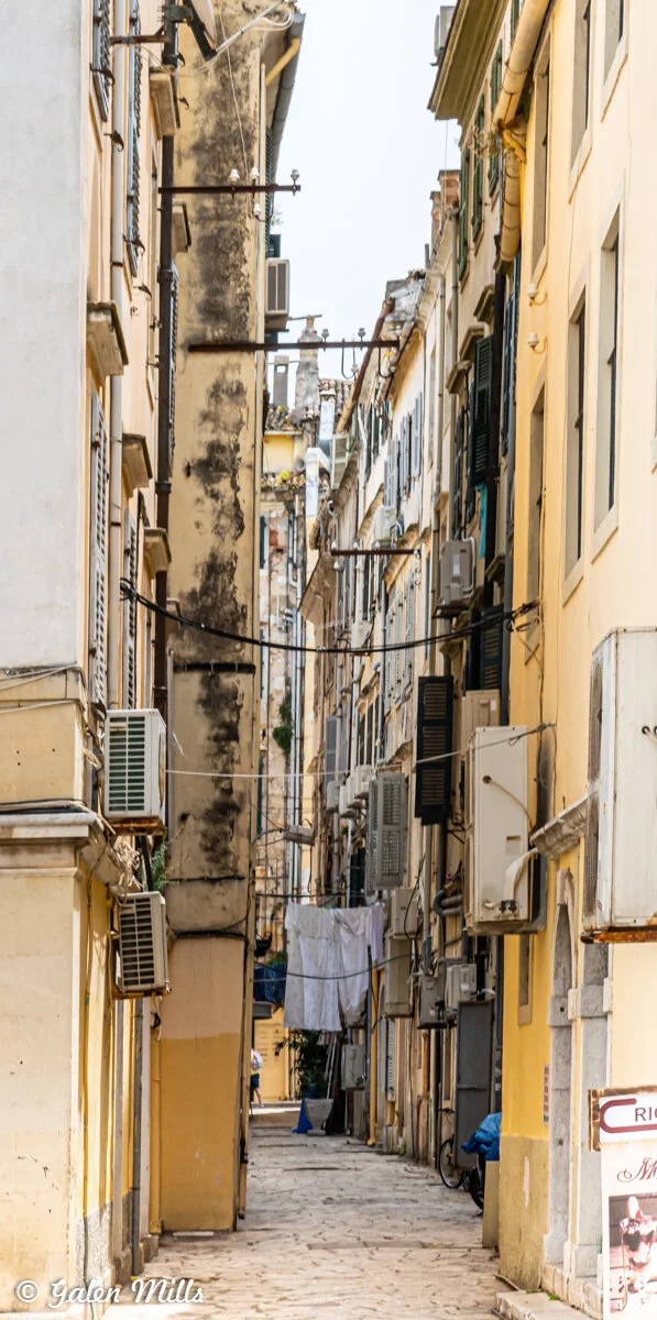 Narrow street with tall buildings, air conditioning units, and hanging laundry.