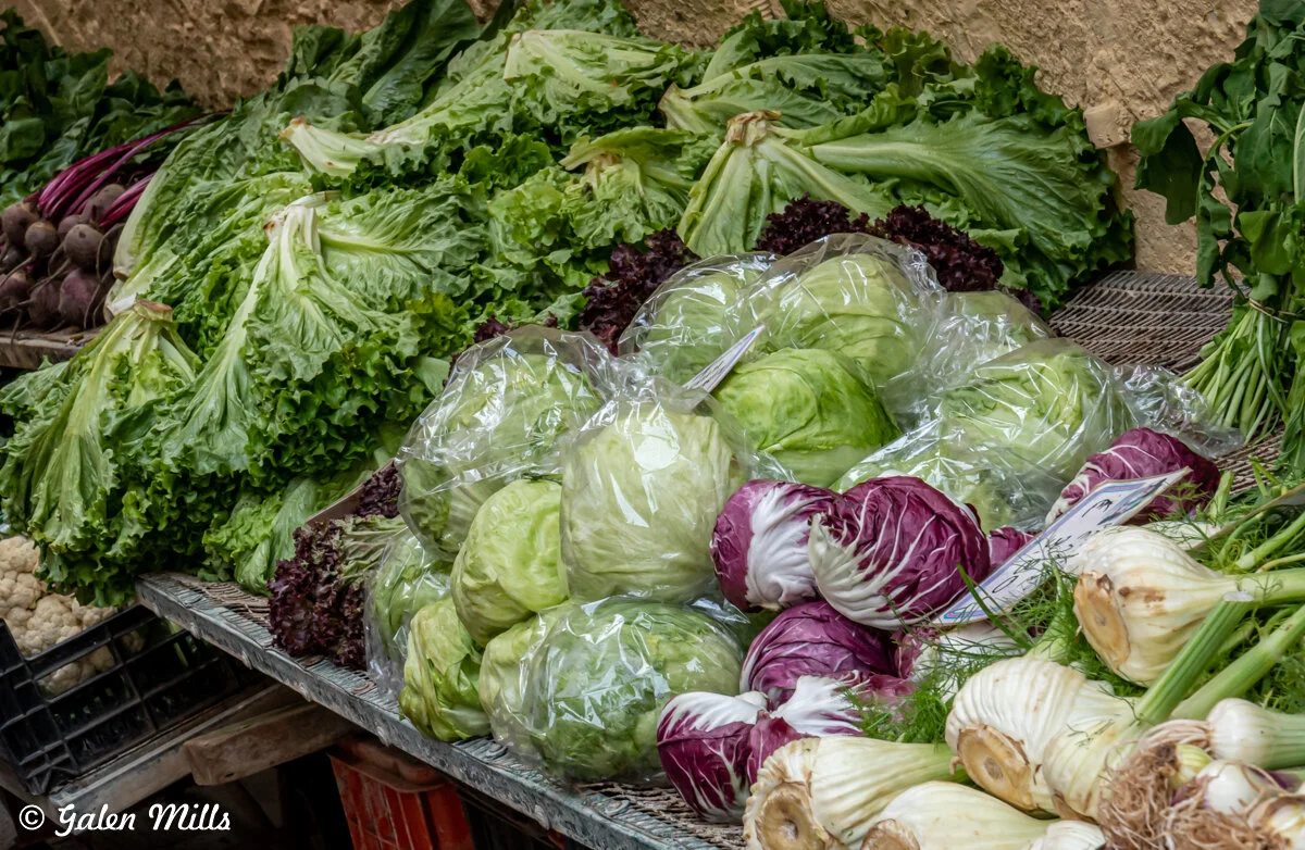 Market stall with leafy greens, cabbage, radicchio, beets, and fennel.