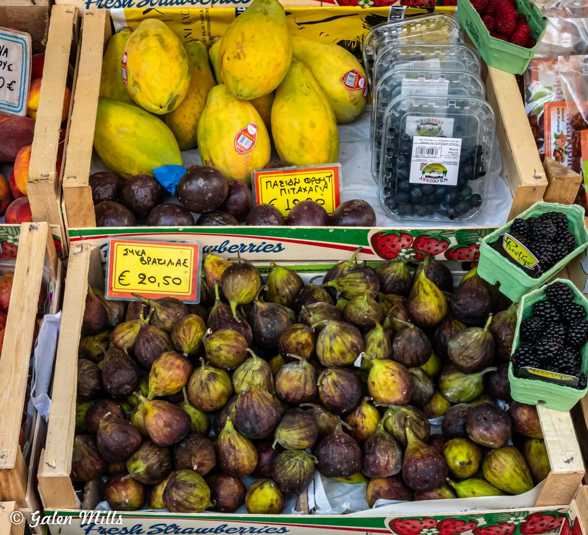 Display of fresh fruits at a market including papayas, figs, blueberries, blackberries, and raspberries.