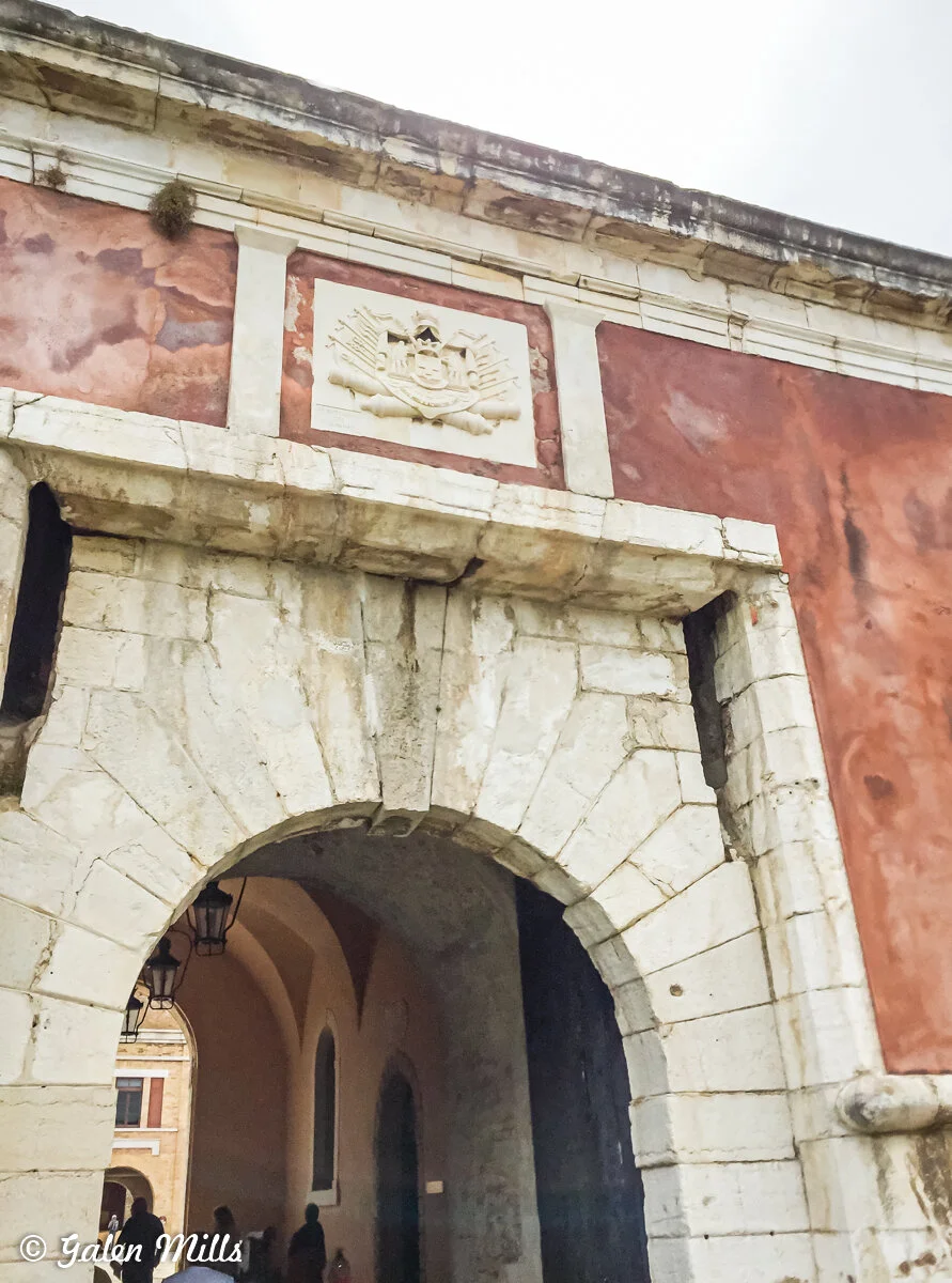 Stone archway with a coat of arms relief above, leading to a courtyard.