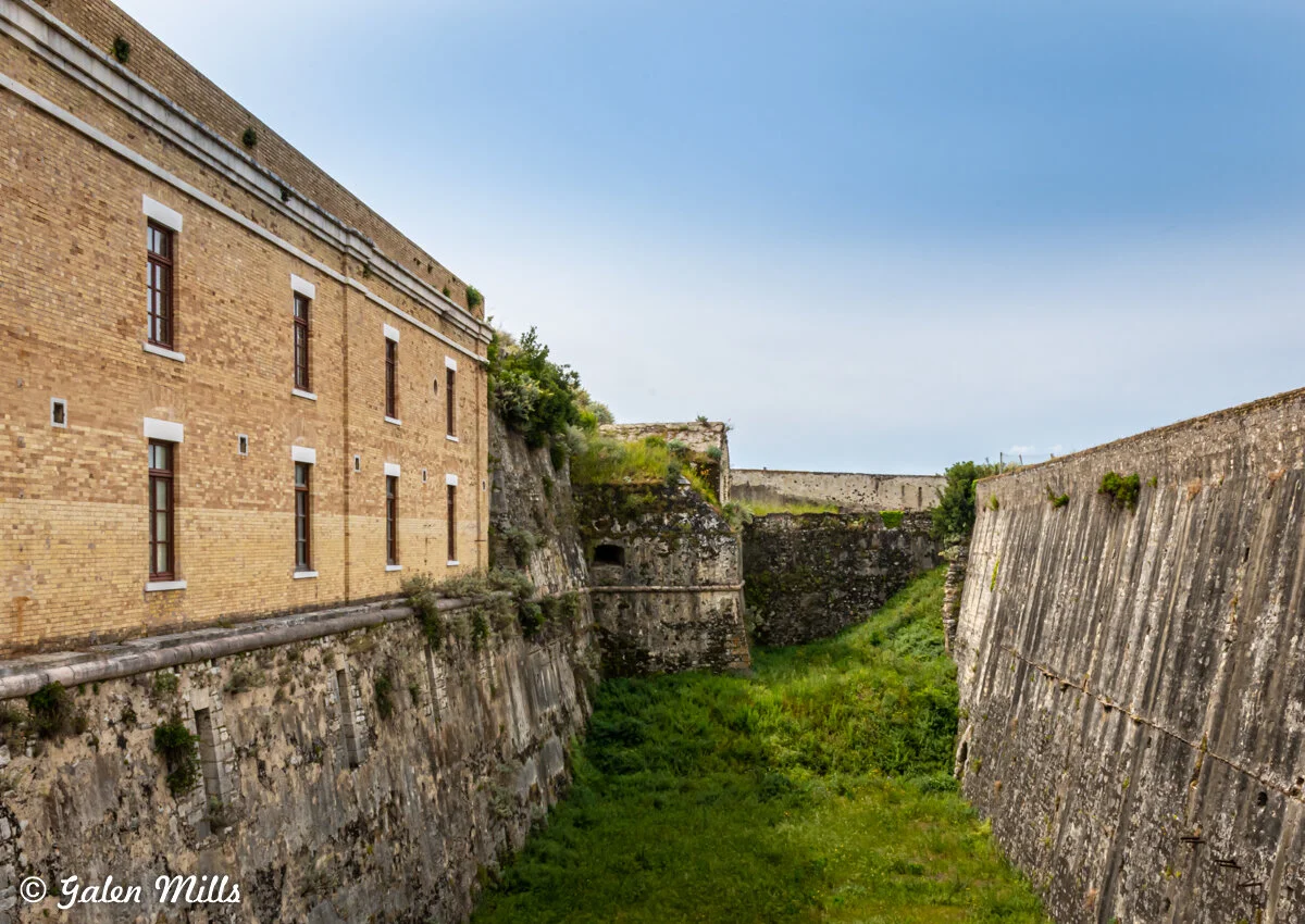 Old brick building next to a stone wall and grassy moat landscape.