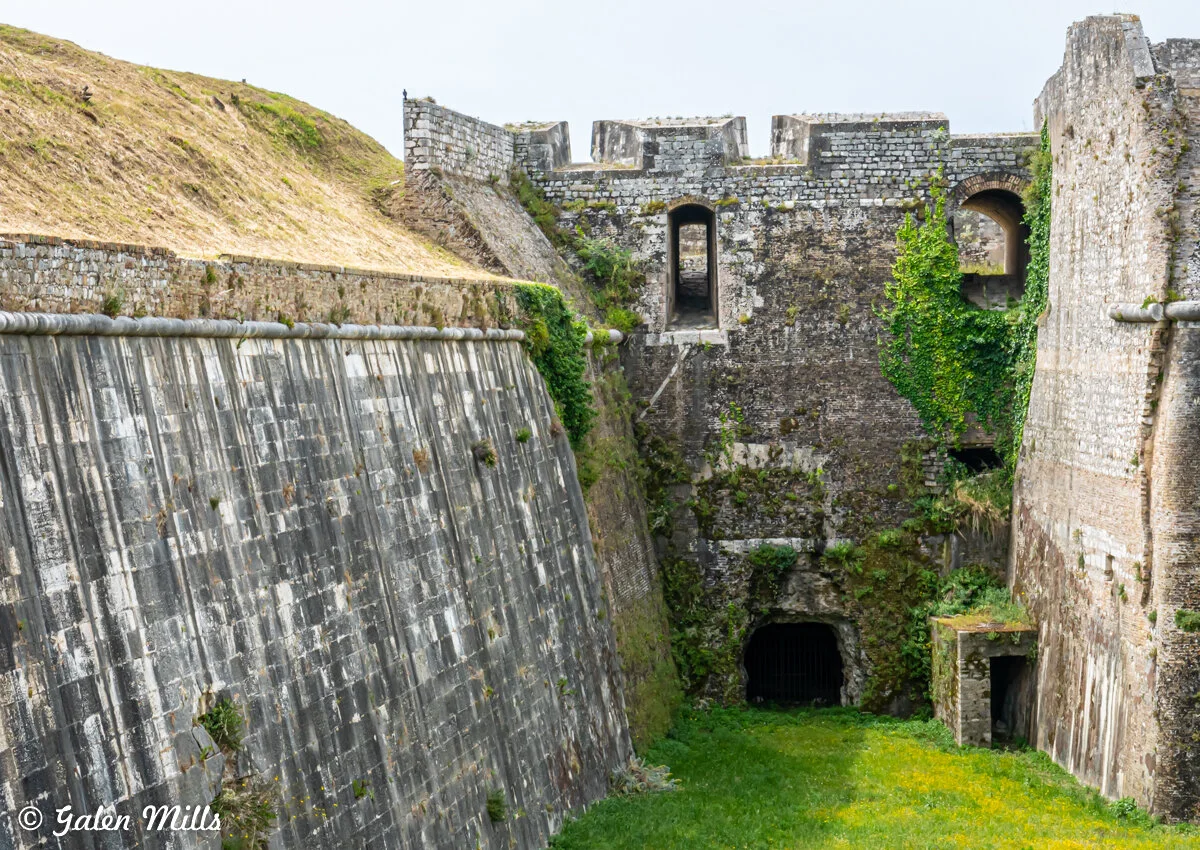 Old stone fort with high walls, ancient arched entrances, and greenery growing on the structure.