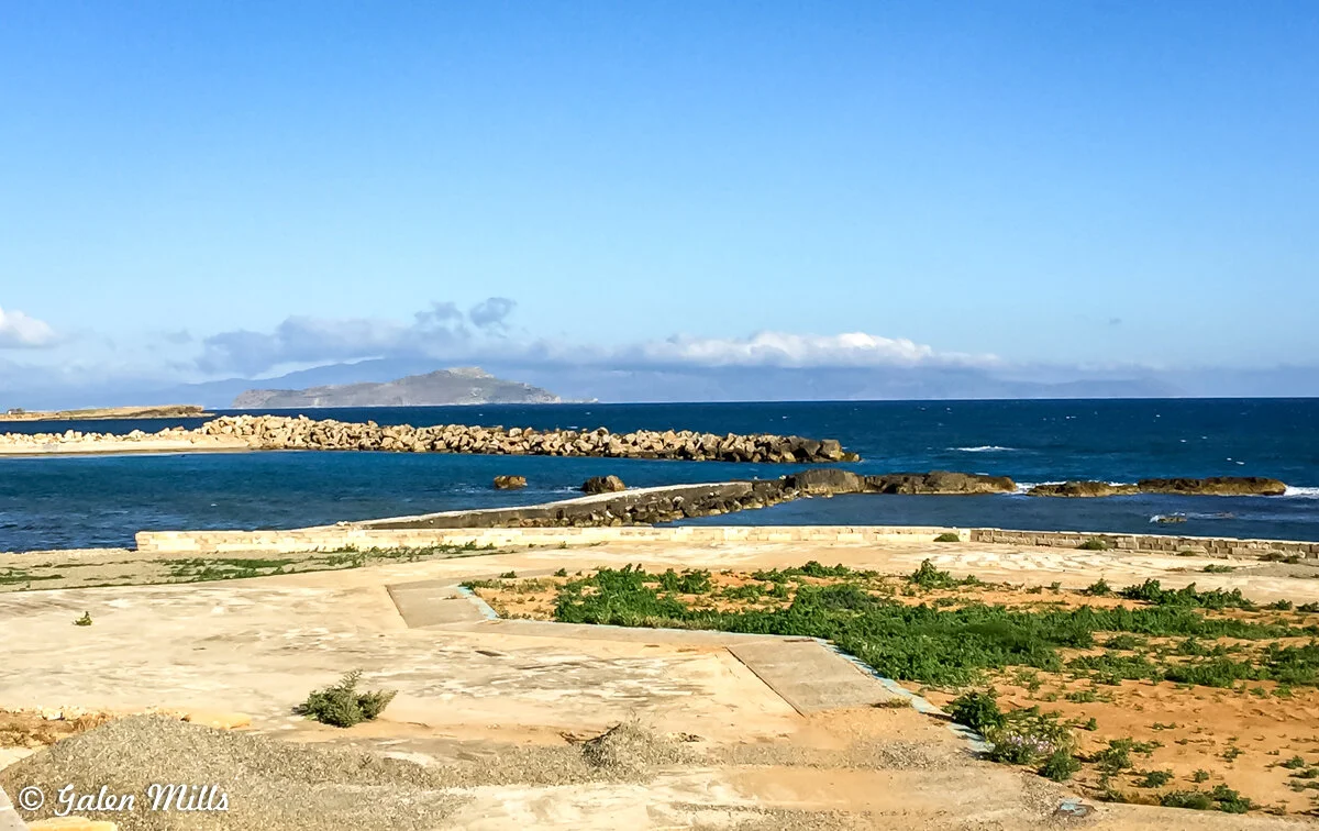 Mediterranean coastal landscape with rocky shoreline, blue sea, distant island, and clear sky