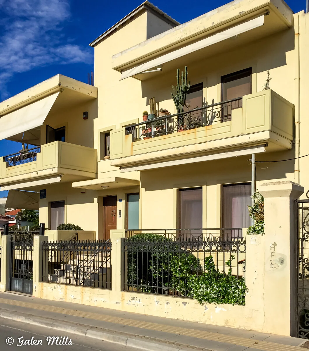 Two-story yellow building with balconies and black wrought iron fencing under a blue sky.
