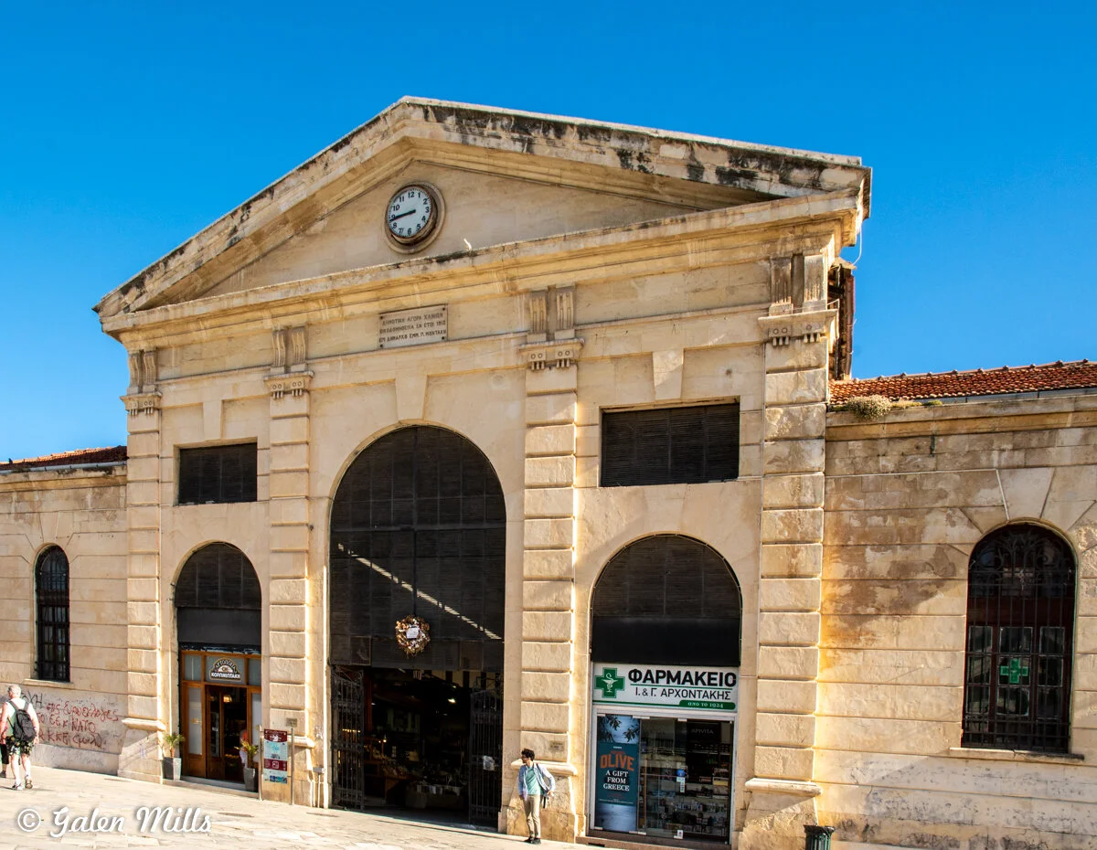 Exterior of old market building with clock, arched entrances, and pharmacy sign