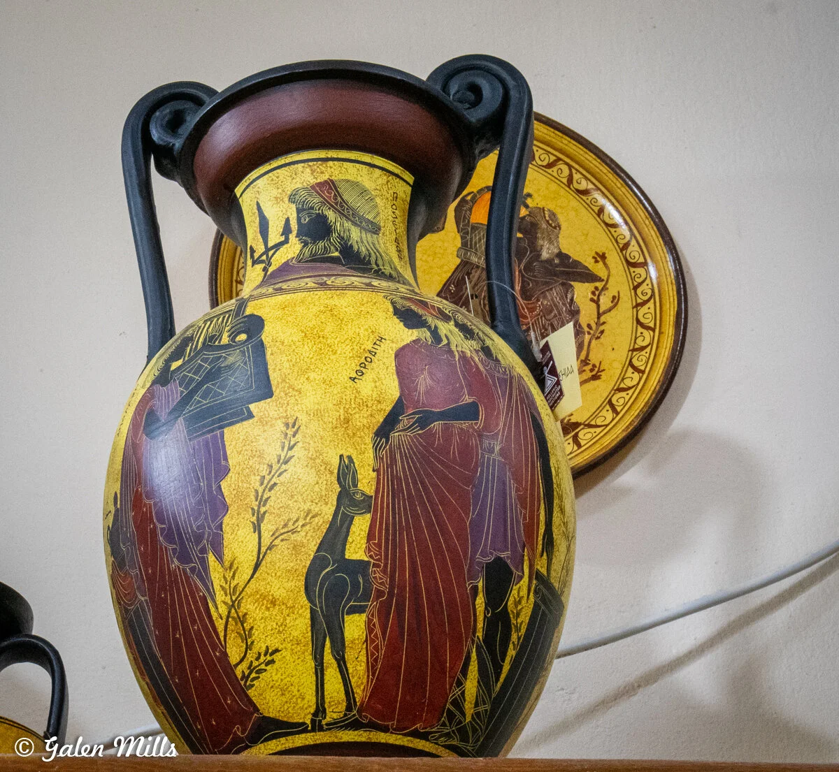 Ancient Greek-style vase with mythological scene and decorative plate in background.