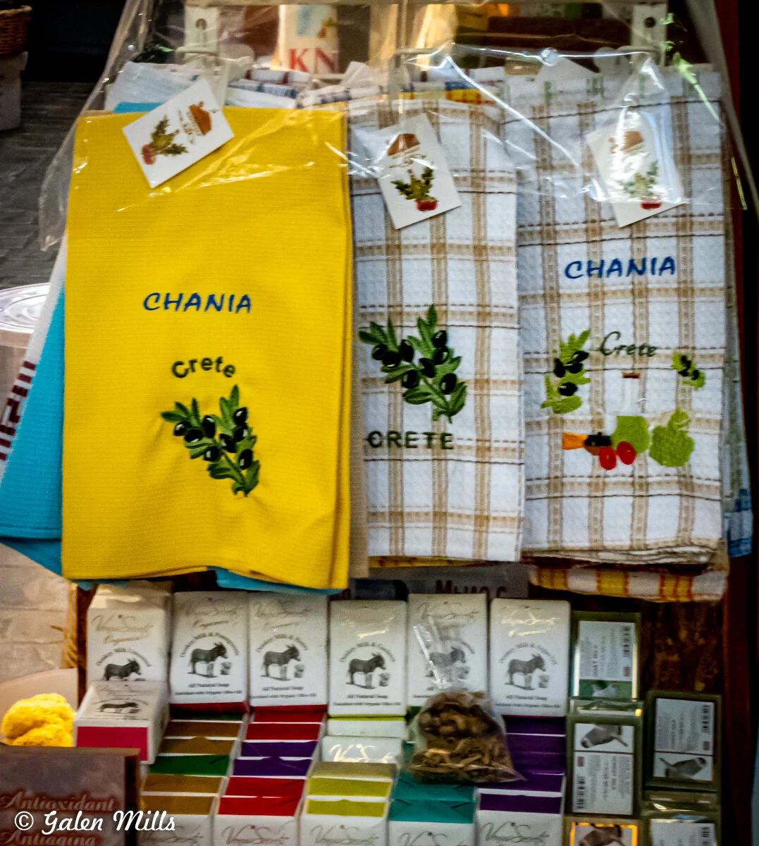 Display of colorful towels with 'Chania Crete' embroidery, alongside boxes of olive oil soap.