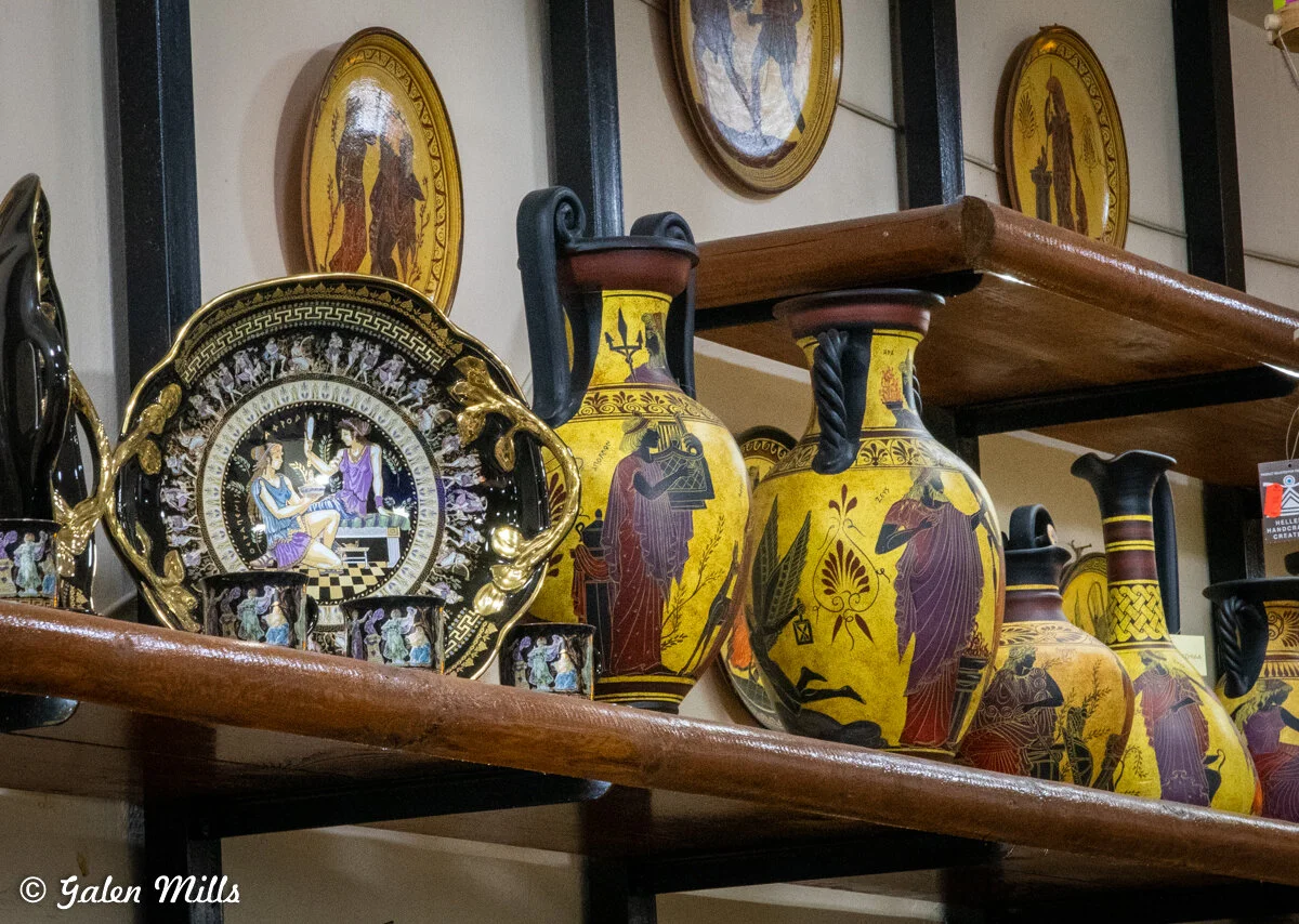 Shelf displaying Greek-style pottery and decorative plates with classical motifs, featuring intricate designs and vibrant colors.