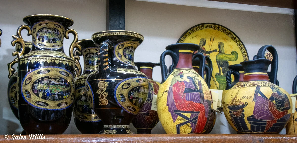 Collection of traditional Greek vases with intricate designs and mythological scenes on a shelf.