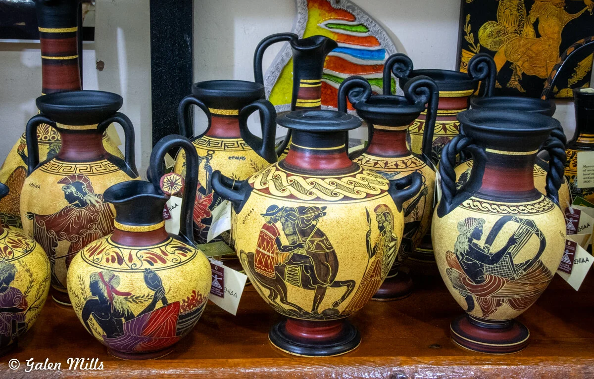 Collection of Greek-style ceramic vases with mythological and decorative motifs on display in a store.