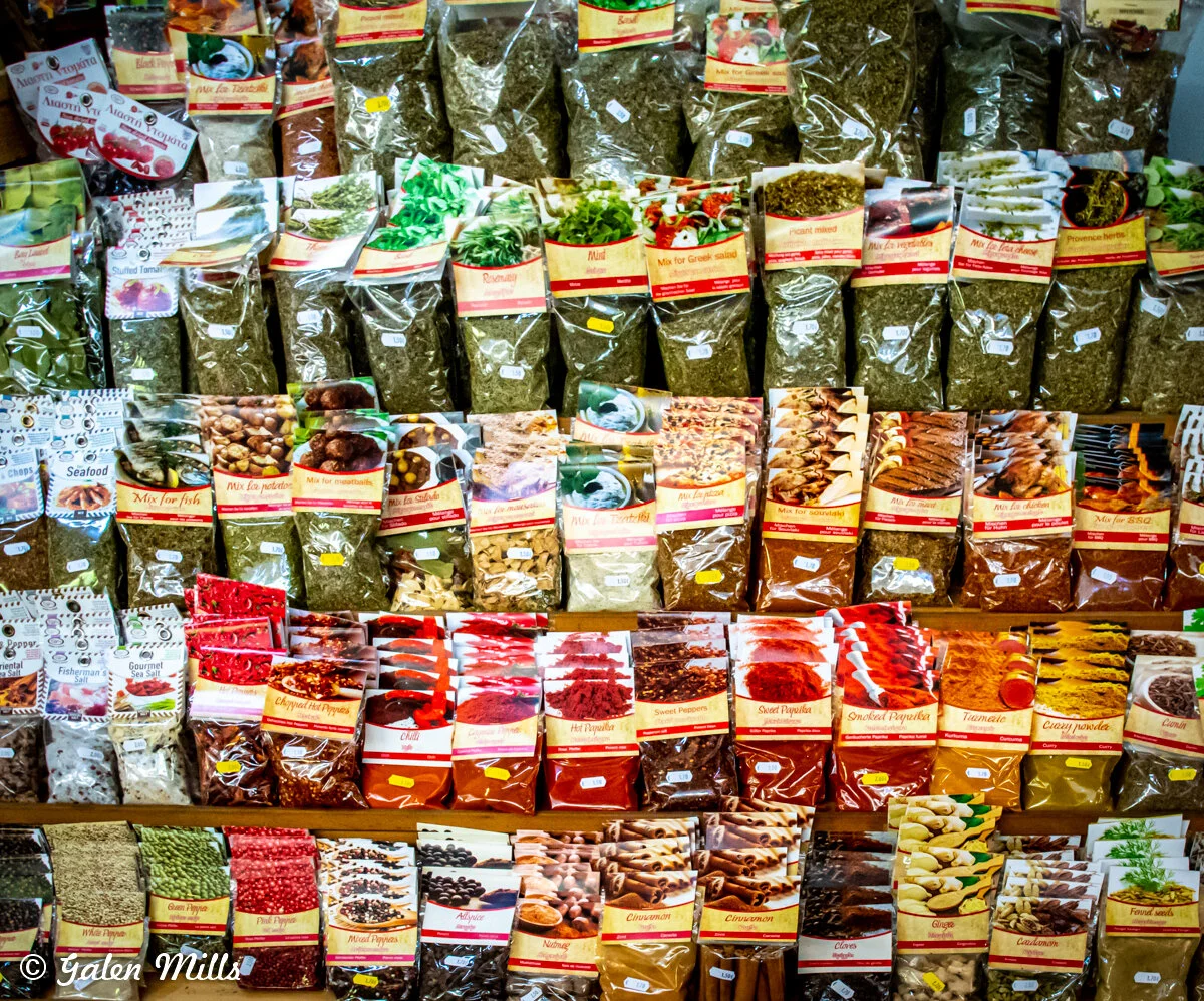 Various packaged spices and herbs, including paprika, cinnamon, and mixed seasoning, displayed on shelves in a market.