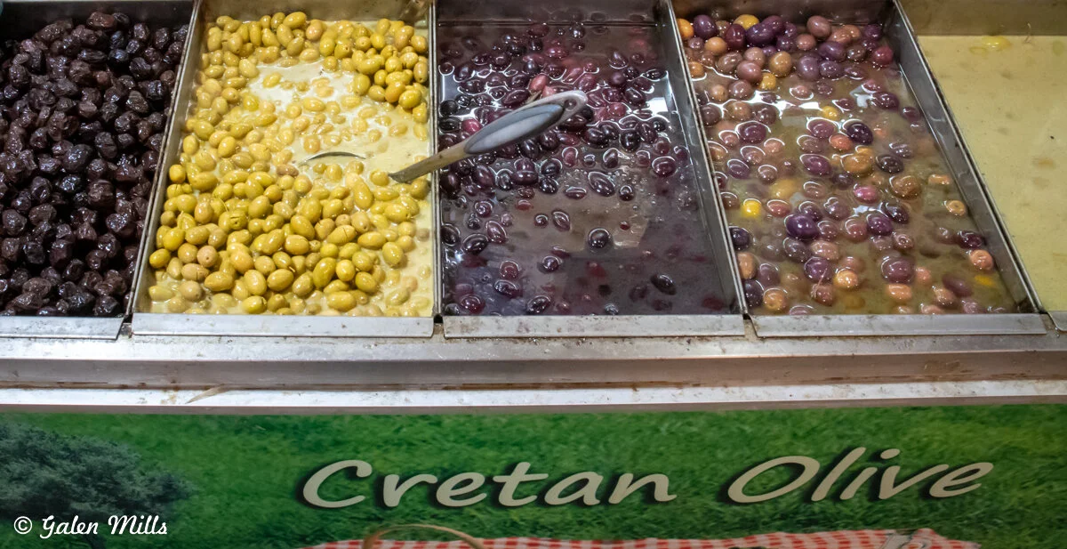 Various types of olives displayed in metal trays labeled 'Cretan Olive'