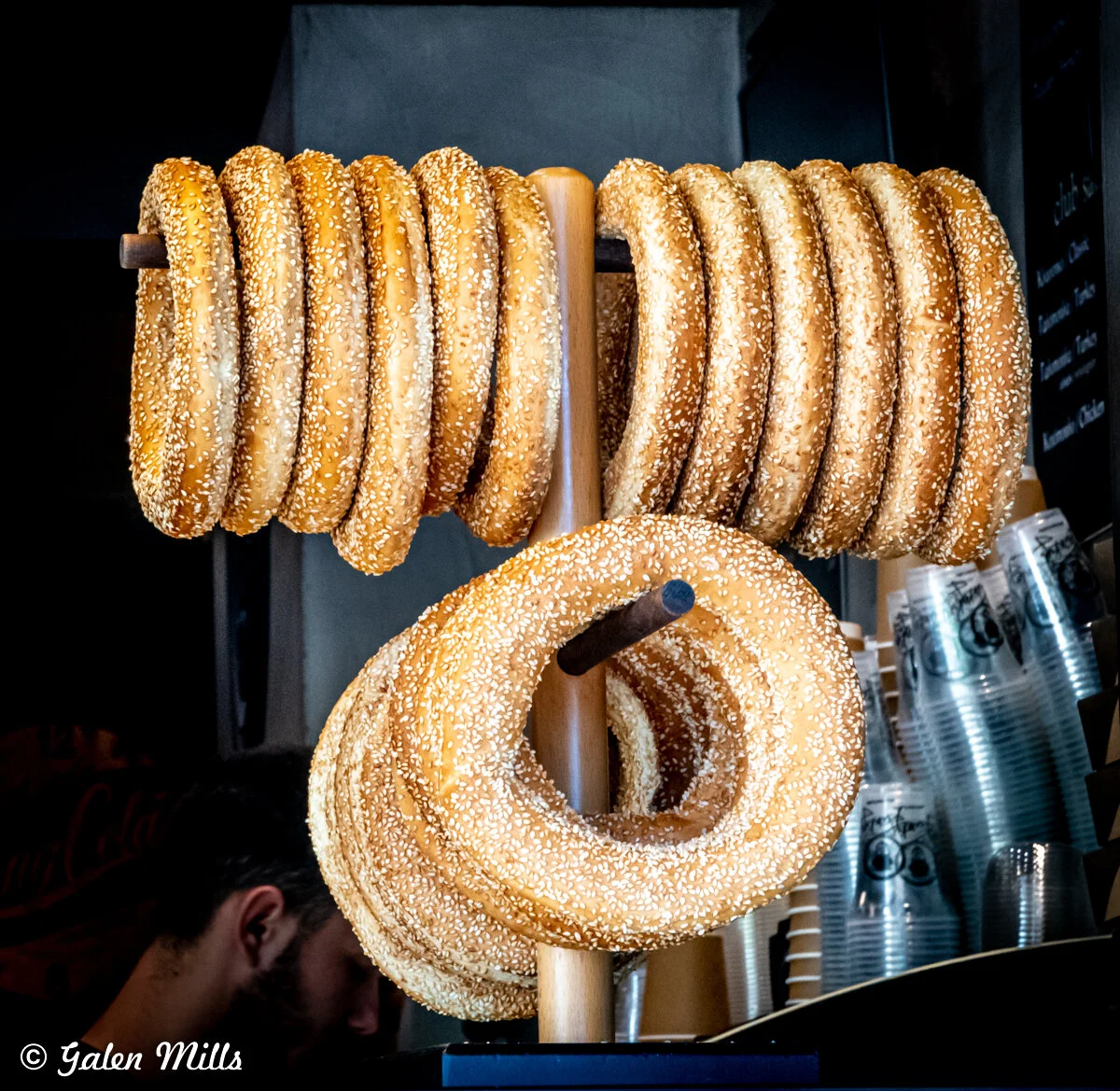 Rows of sesame seed-covered bagels on a wooden pole display.