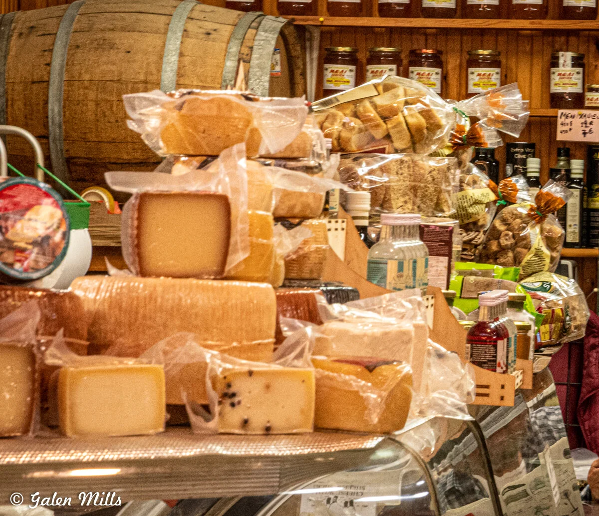 Assorted cheeses and packaged goods on a deli counter with wooden shelves in the background.
