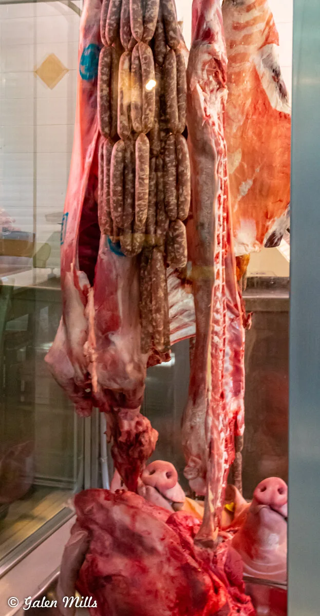 Hanging meat cuts and sausages in a butcher shop display.