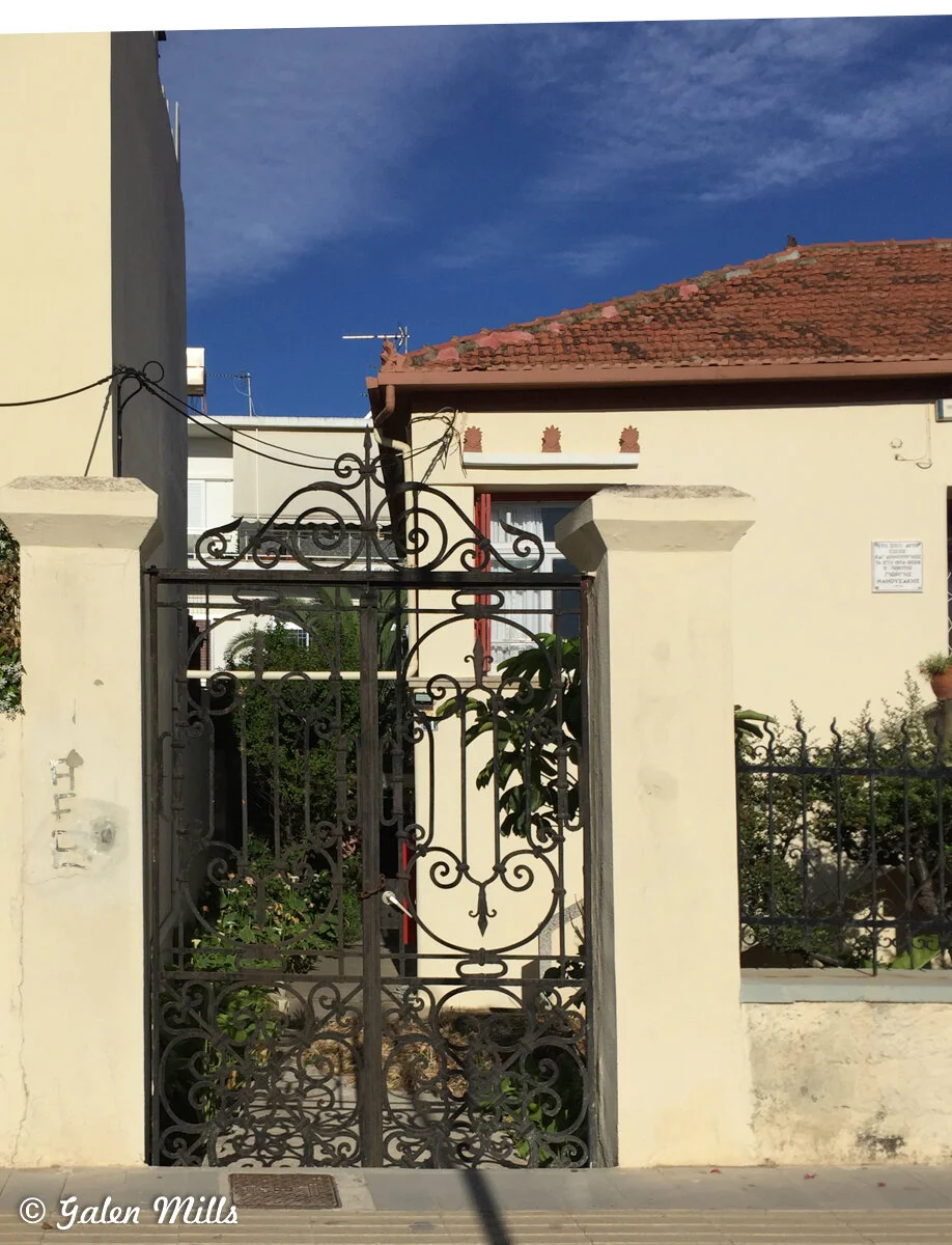 Ornate metal gate in front of a Mediterranean-style house with red-tiled roof.
