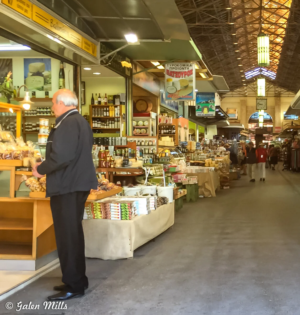 Indoor market with various stalls selling food and products, people shopping, and a high ceiling with lights.