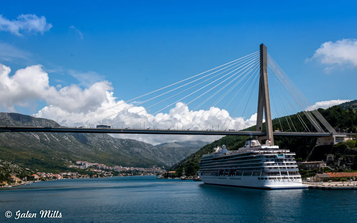 Cruise ship near Franjo Tuđman Bridge in Dubrovnik, Croatia, with mountains and blue sky.