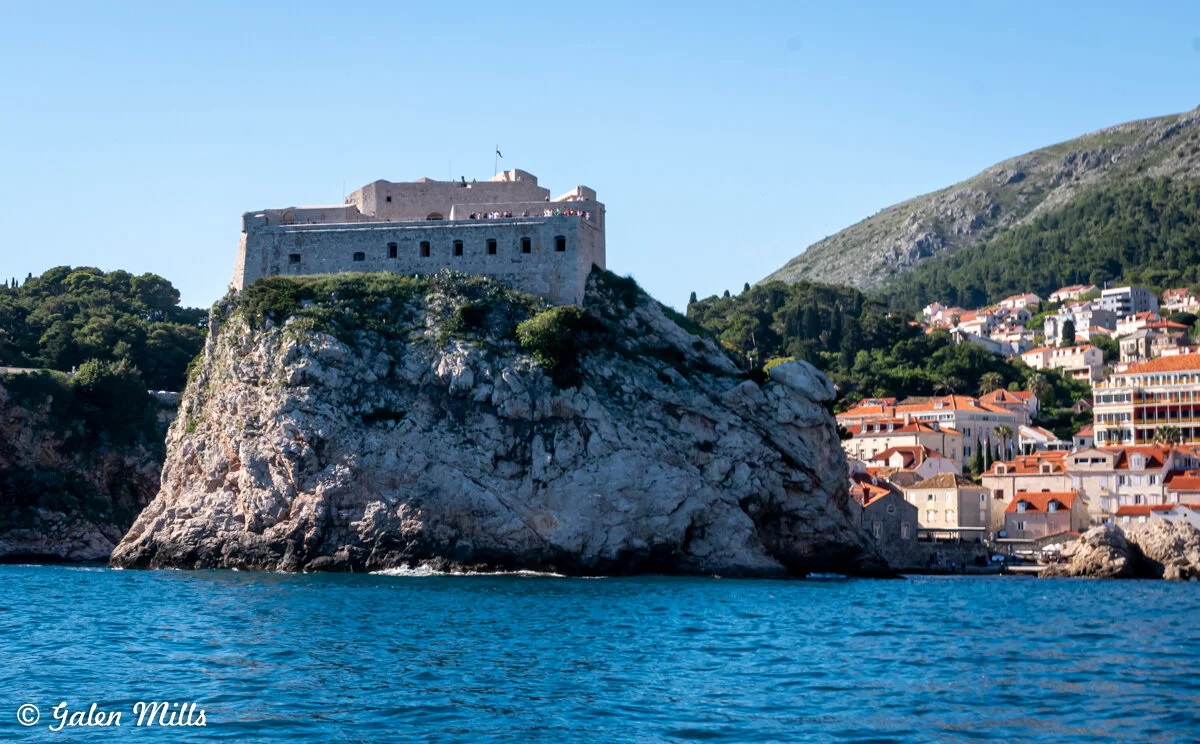 Fortress on rocky cliff by the sea in Dubrovnik, Croatia with surrounding buildings and trees.