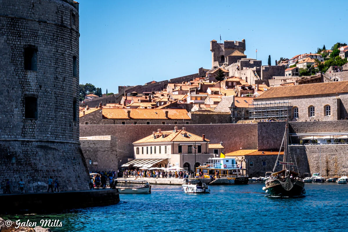 Historic stone fortress and buildings in Dubrovnik, Croatia with boats in the harbor and clear blue sky.