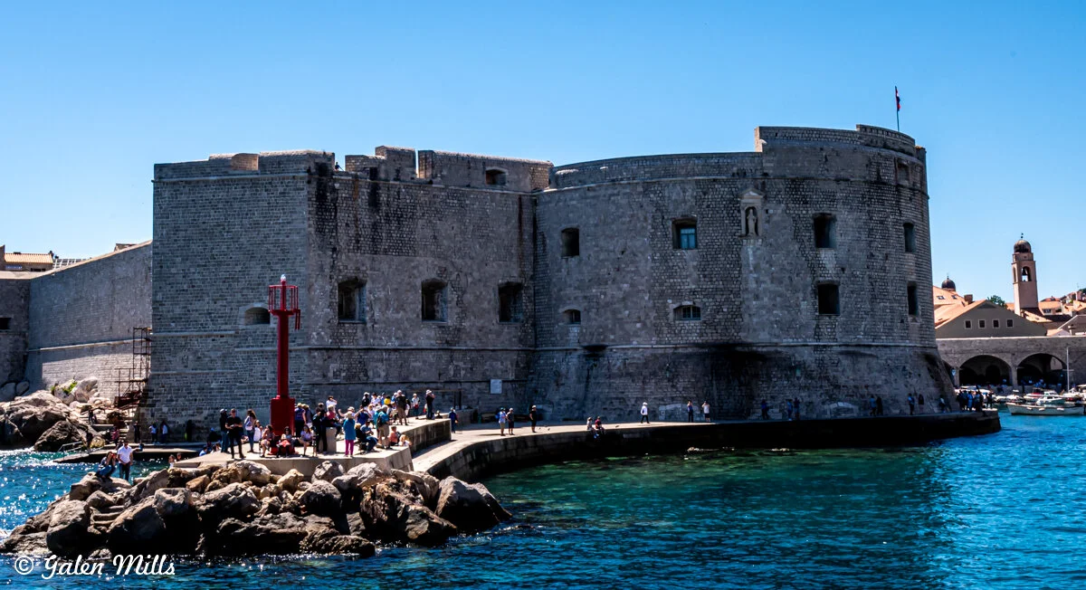 Historical fortification on a harbor with tourists, blue sky, and clear water.