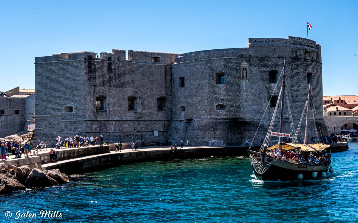 Stone fortress by the water with a boat labeled 'Panorama Cruise' in Dubrovnik, Croatia.