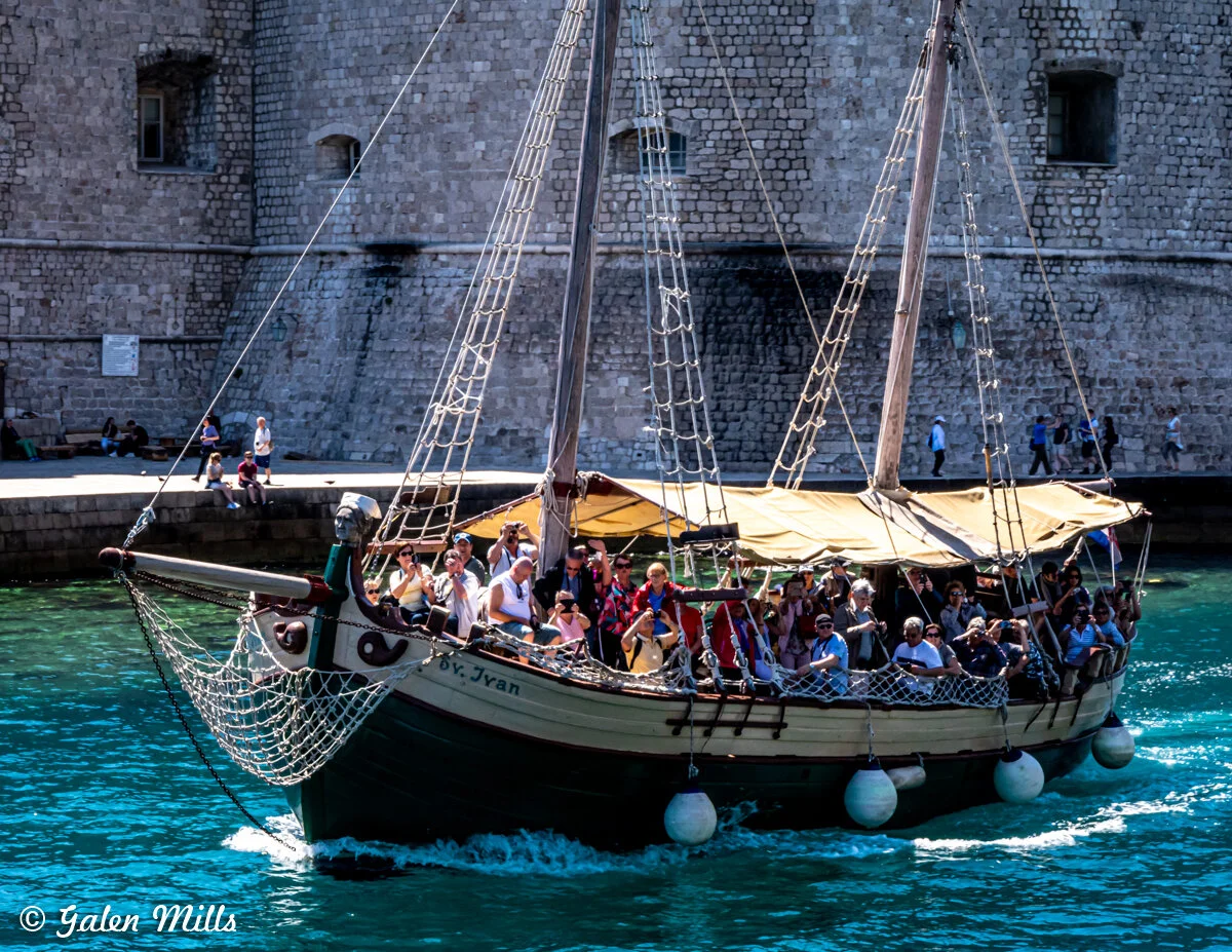 Tourist ship with people sailing near stone fortress, bright blue water