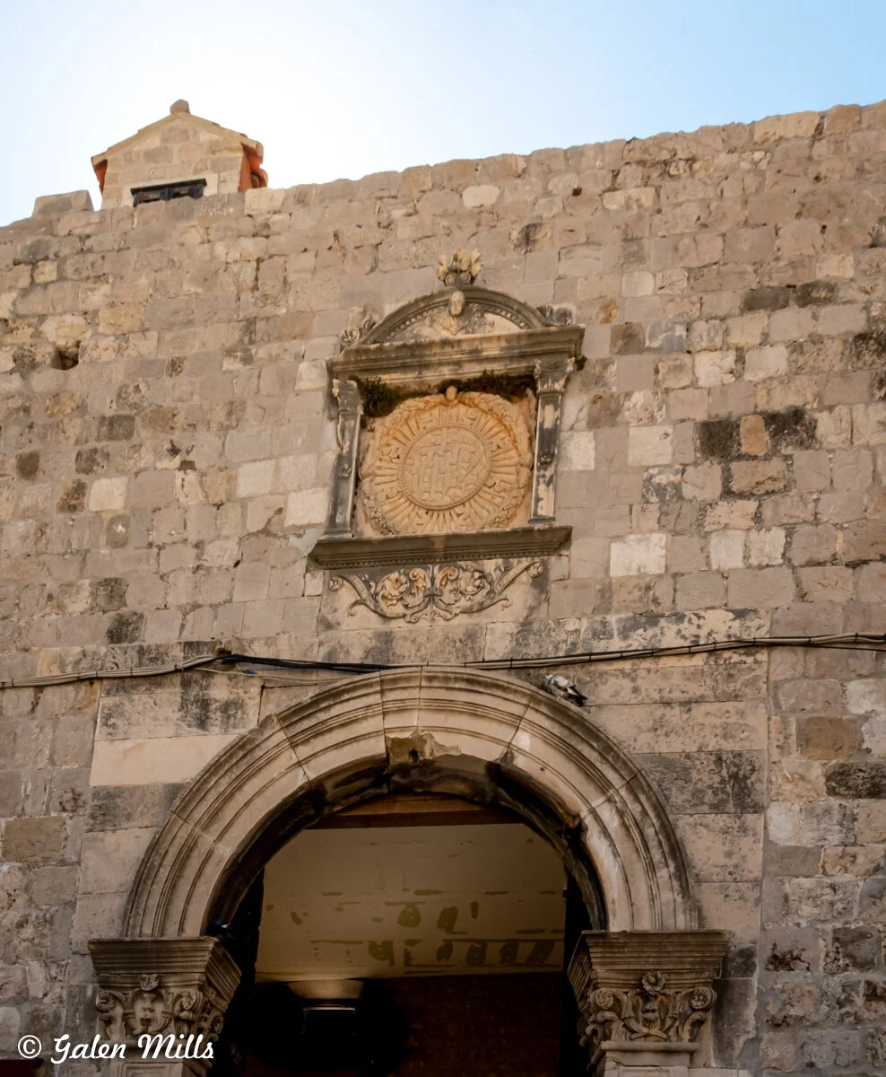Stone wall with ornate archway and decorative emblem.