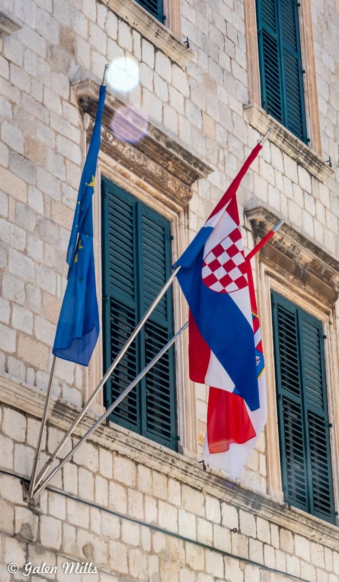 Flags of the European Union and Croatia on a stone building with green shutters.