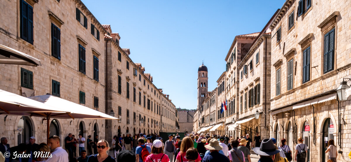 Crowded street in Old Town Dubrovnik with historic buildings and bell tower.