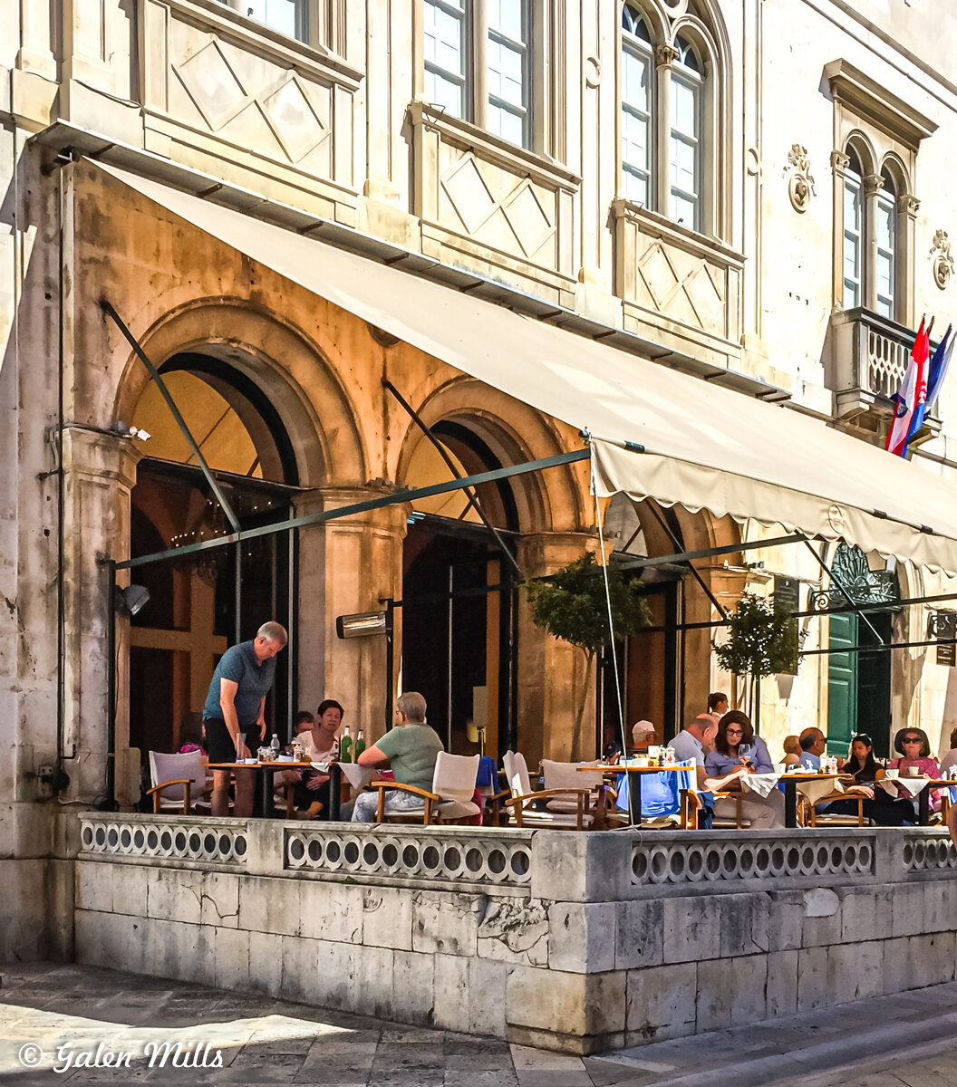 Outdoor cafe with people dining under a canopy next to a historic building.