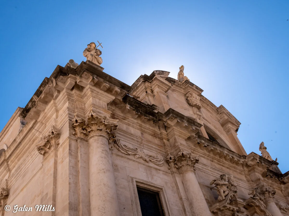 Baroque cathedral architecture with statues and columns against a blue sky