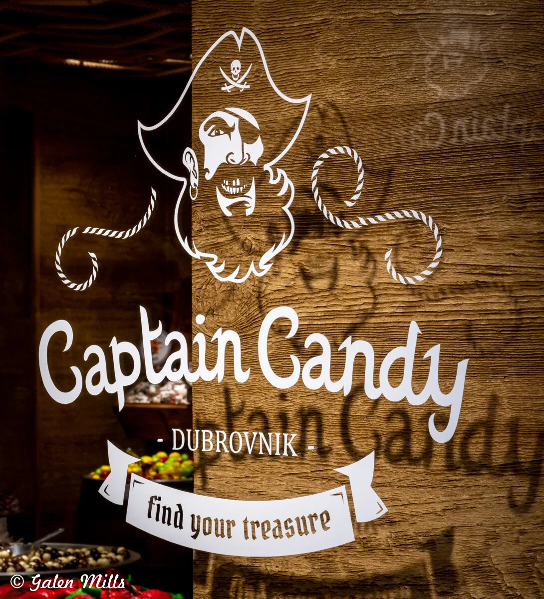 Captain Candy logo on a wooden wall with a pirate design, located in Dubrovnik. Slogan reads 'find your treasure' with candies visible below.