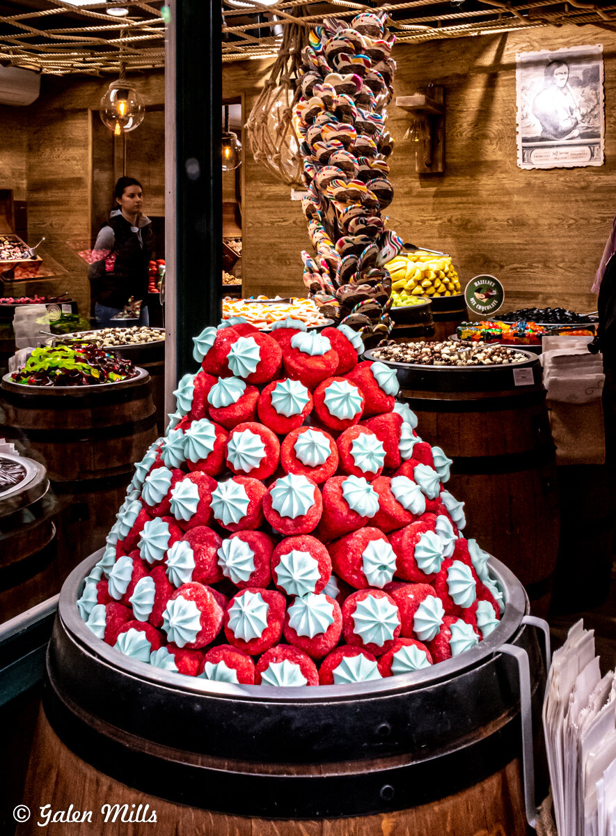 A display of colorful candies in a shop, featuring pyramids of red candies with blue tops and a spiral of multicolored lollipops.