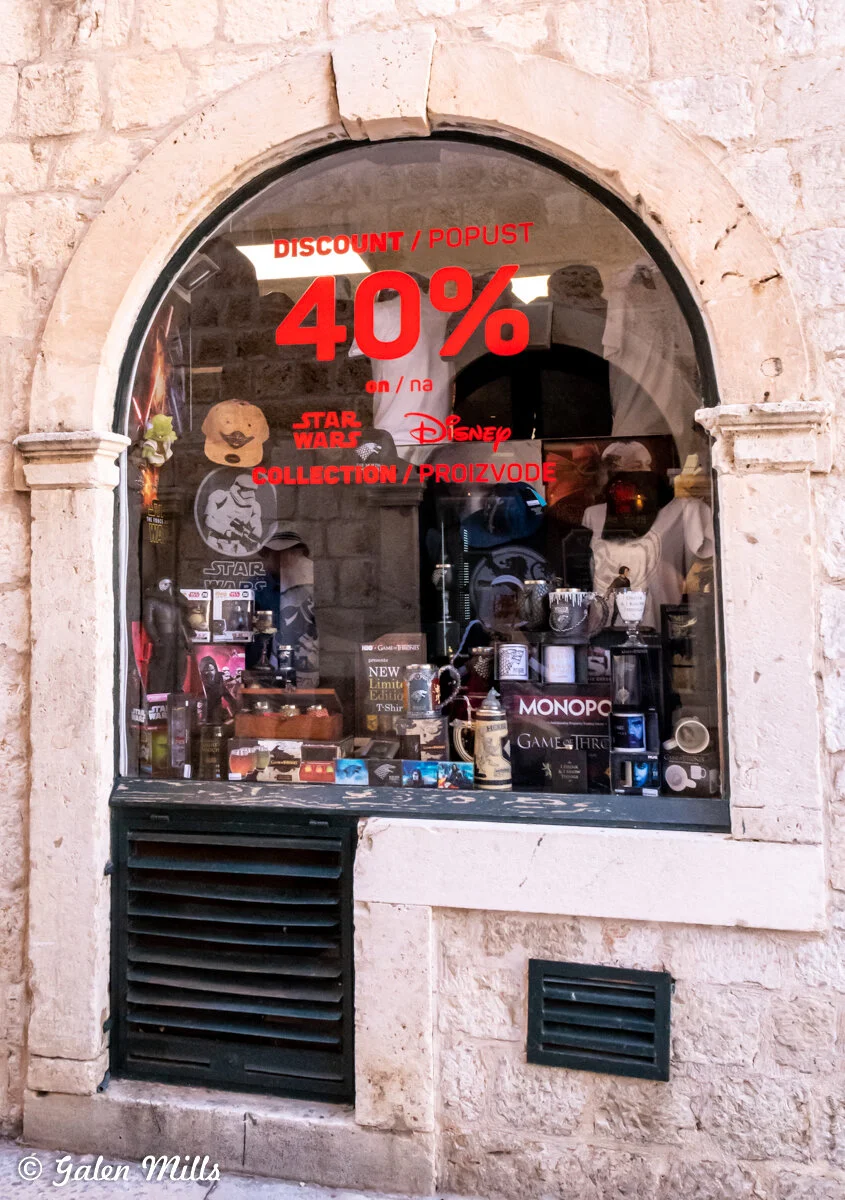 Shop window with a 40% discount sign for Star Wars and Disney merchandise, various collectibles and toys displayed, stone wall surround.