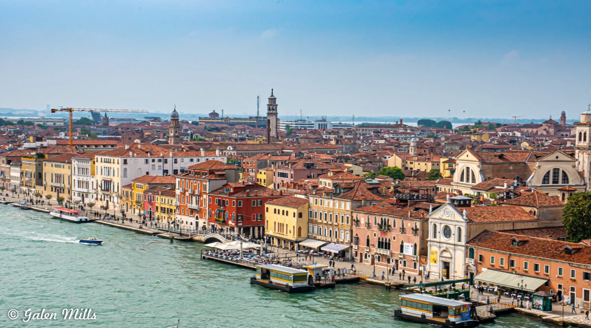 Scenic view of Venice with colorful buildings along a canal, featuring a mix of architectural styles, a bell tower, and boats on the water.