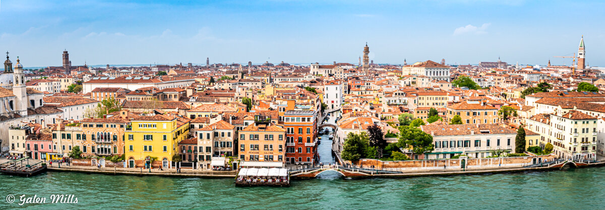 Panoramic view of Venice, Italy, featuring buildings with red roofs along a canal under a clear blue sky.