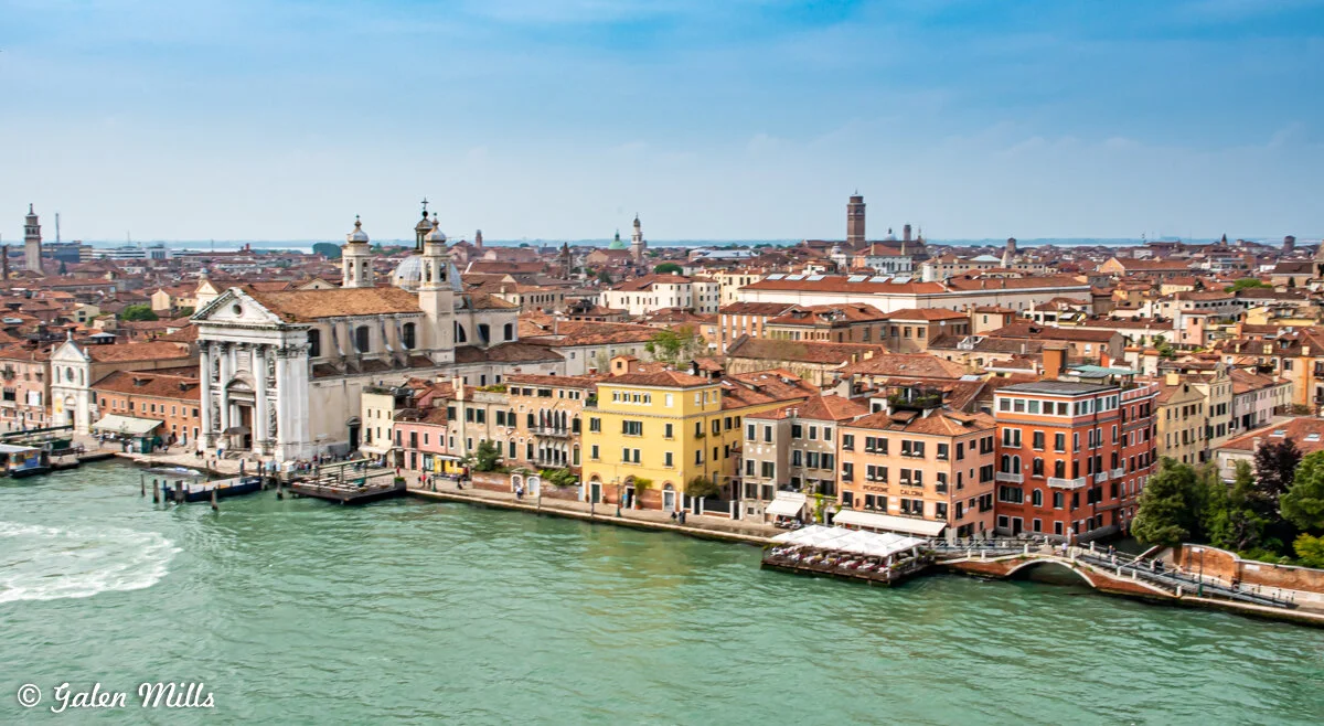 Aerial view of Venice, Italy, featuring historic buildings, a prominent church, and a canal with teal water.