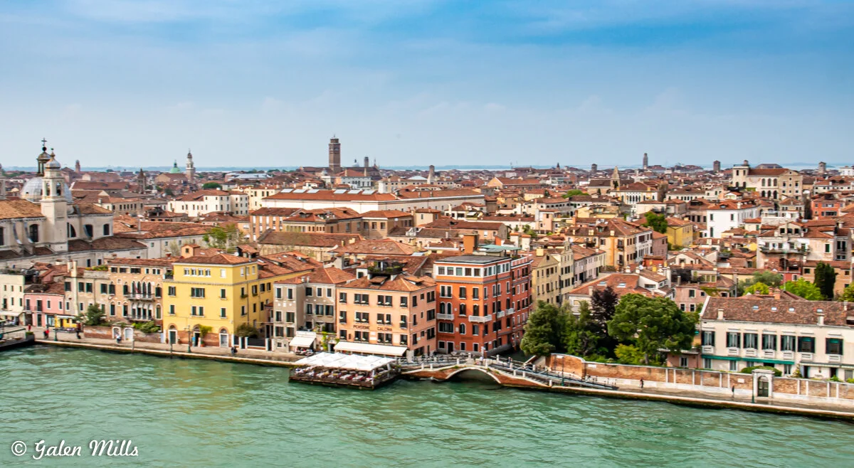 Aerial view of Venice, Italy with colorful buildings, canals, and a bridge under a blue sky.