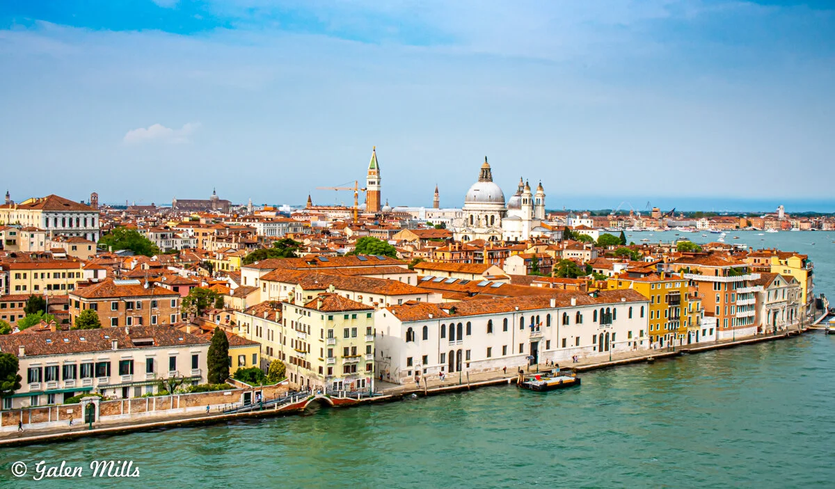 Aerial view of Venice, Italy, showcasing historic buildings with red-tiled roofs, the Grand Canal, and the prominent dome of Santa Maria della Salute.