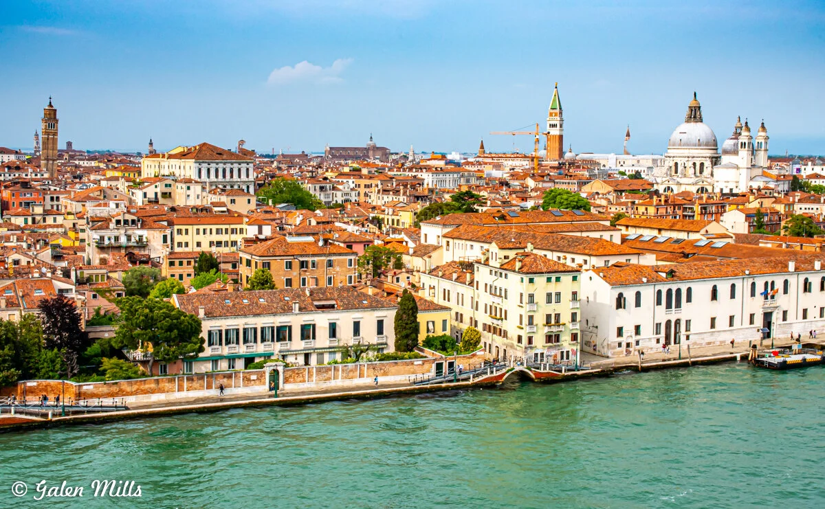 Aerial view of Venice, Italy, showcasing historic buildings with red-tiled roofs, the Grand Canal, and prominent landmarks like the Basilica di Santa Maria della Salute and St Mark's Campanile.
