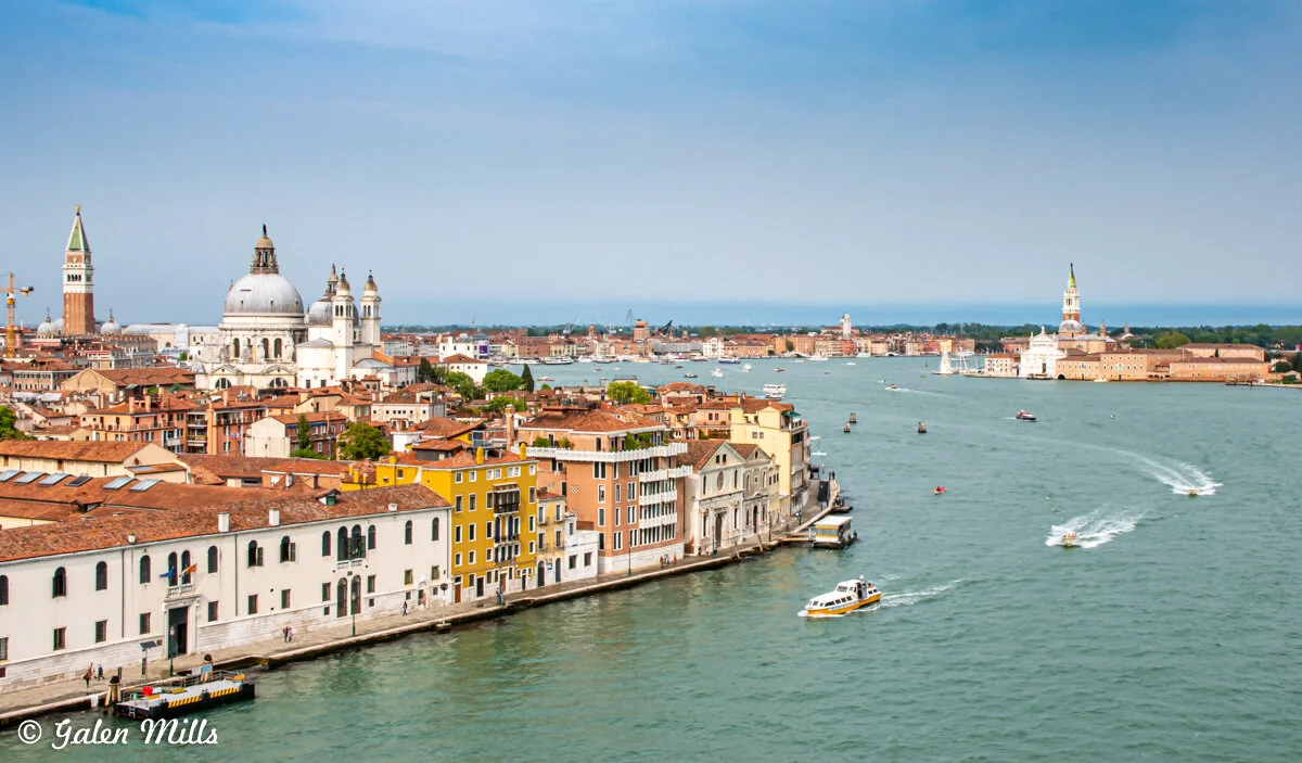 Scenic view of Venice, Italy featuring the Grand Canal, colorful buildings, and boats on the water. Prominent landmarks include the domed church and bell tower.